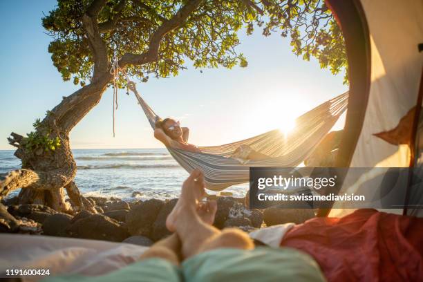 standpunt van de voet van de mens van binnen een tent camping op het strand in hawaï kijken naar vriendin in hangmat buitenshuis - journey pov stockfoto's en -beelden
