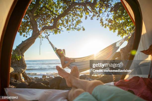 point of view of man's feet from inside a tent camping on the beach in hawaii looking at girlfriend in hammock outdoors - 2 point perspective stock pictures, royalty-free photos & images