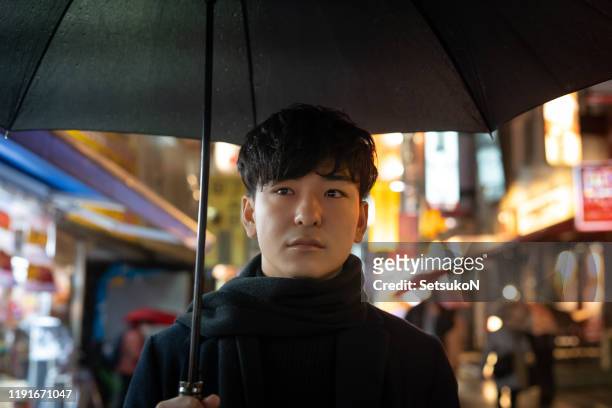 young asian man in the rain - holding umbrella stock pictures, royalty-free photos & images