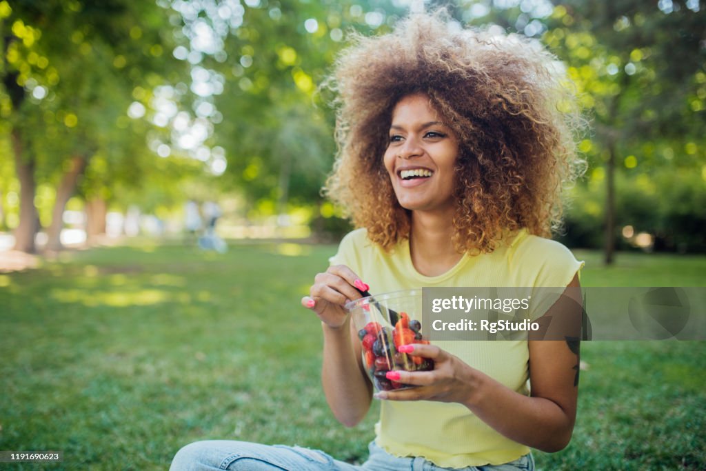 Beautiful girl resting on the grass and eating fruit salad