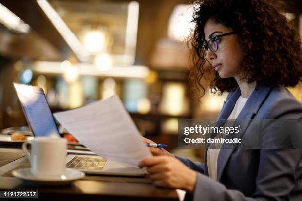 businesswoman working on laptop at a cafe - reviewing paperwork stock pictures, royalty-free photos & images