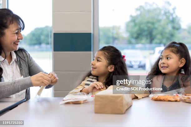 teacher helps elementary students during lunch - elementary school cafeteria stock pictures, royalty-free photos & images