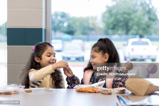tweeling zusters delen lunch in de school cafetaria - school lunch stockfoto's en -beelden