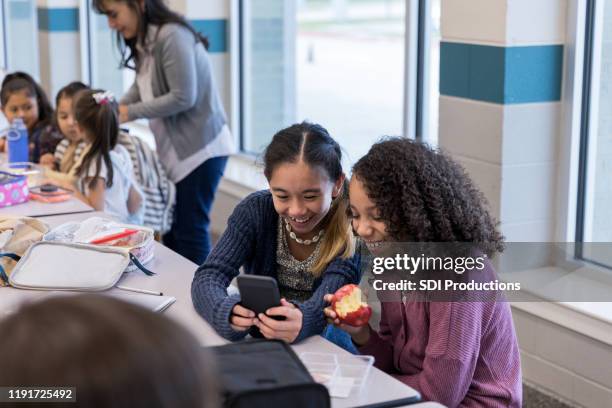 elementary school female friends laugh at photos on smart phone - middle school lunch stock pictures, royalty-free photos & images