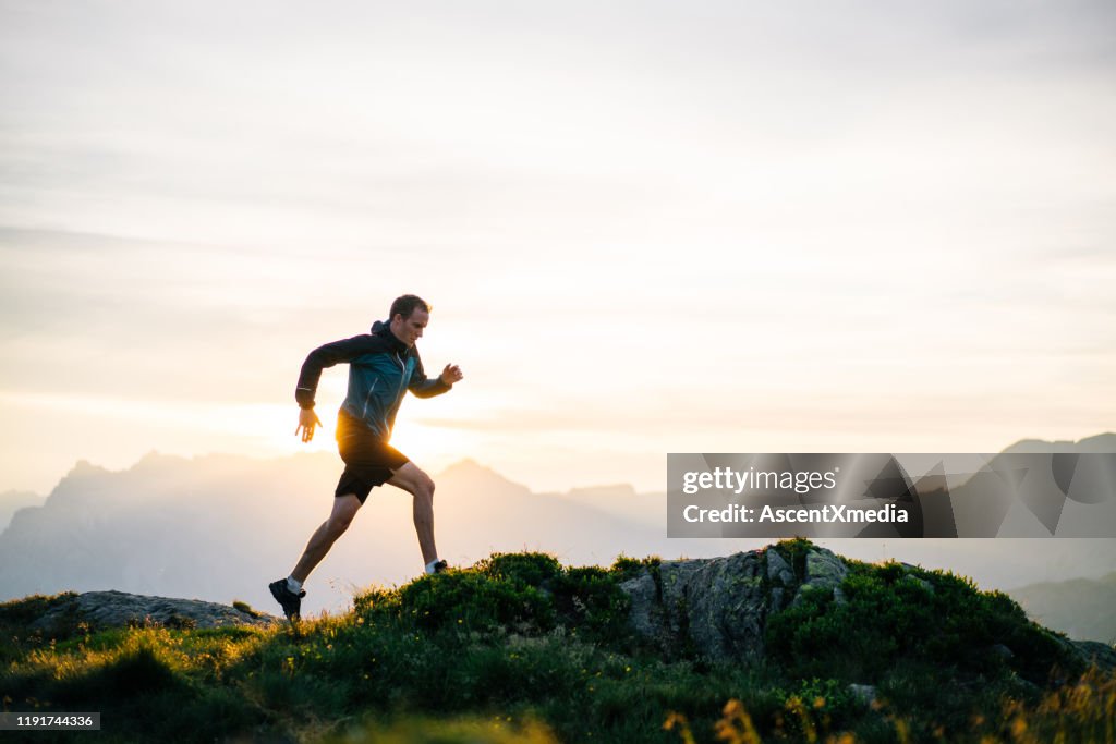 Junger Mann rennt bei Sonnenaufgang auf Bergrücken