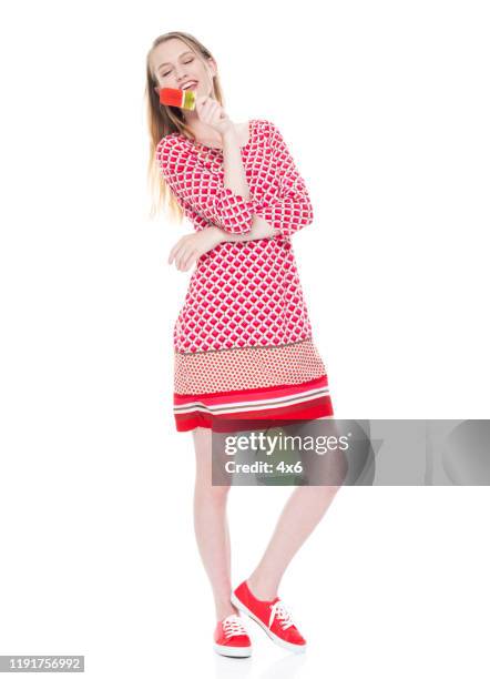 Full length / one person / front view of 18-19 years old adult beautiful blond hair caucasian female / young women teenage girls standing wearing dress who is smiling / happy / cheerful / cool attitude and holding ice cream / dessert / popsicle stick