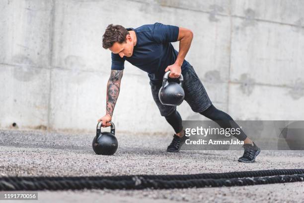 caucasian male athlete doing kettlebell plank row exercise - kettle bells stock pictures, royalty-free photos & images
