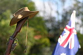 Close-up of an upturned Australian 303 rifle butt upon which sits a traditional Australian Slouch Hat with rising sun badge, dogtags and the Australian National Flag on ANZAC Day