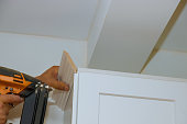 Carpenter nailing crown moldings in the kitchen cabinets framing trim worker using brad nail gun