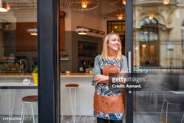 young cafe owner standing with arms crossed at front door - store window stock pictures, royalty-free photos & images