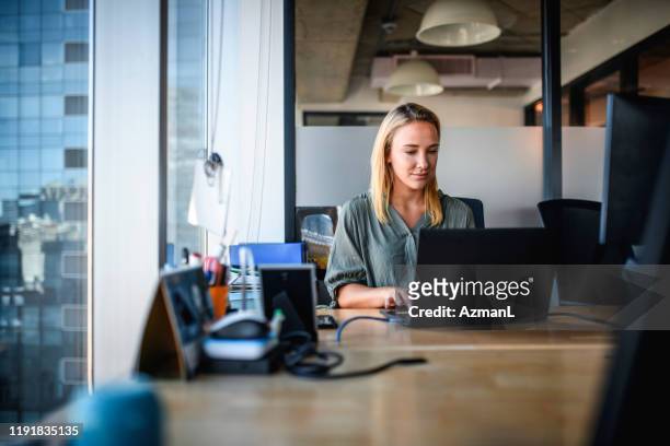 giovane imprenditrice focalizzata che lavora sul laptop in office - scrivania foto e immagini stock