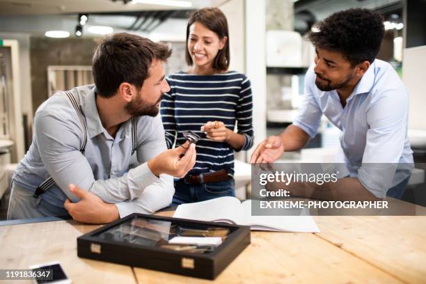 sales rep having a discussion with young shopping couple while leaning on the table with a catalog in the store. - customer experience stock pictures, royalty-free photos & images