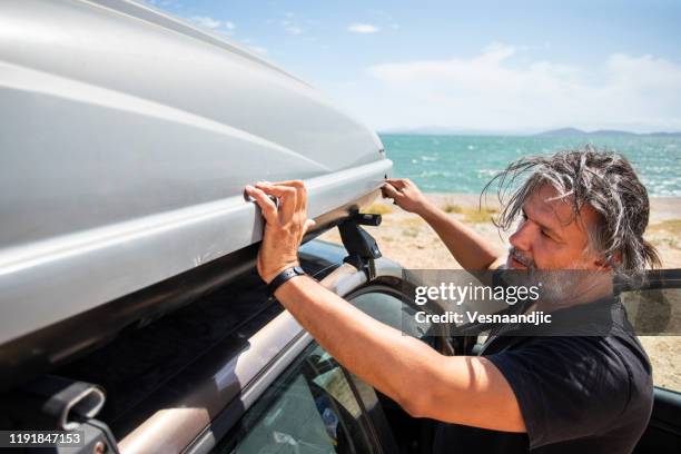 männer packen cargo box container auf dachträger im urlaub - gepäckablage stock-fotos und bilder