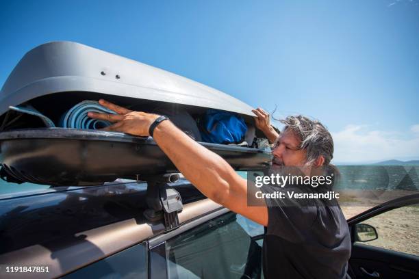 männer packen cargo box container auf dachträger im urlaub - car roof box stock-fotos und bilder