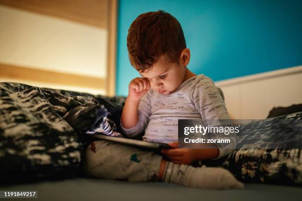 sleepy boy uses digital tablet in bed - kid rubbing eyes stock pictures, royalty-free photos & images