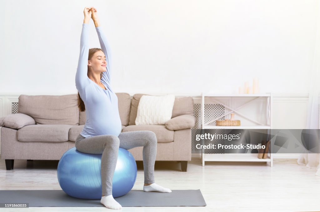 Young pregnant girl sitting on fit ball at home