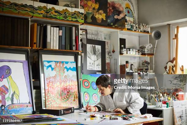 man with down syndrome painting in studio - international artists stock pictures, royalty-free photos & images