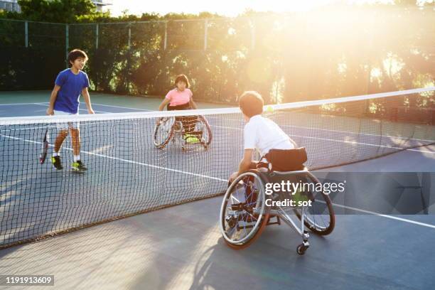 a young male in a wheelchair playing tennis with a young female in a wheelchair and a young male - wheelchair tennis stock pictures, royalty-free photos & images