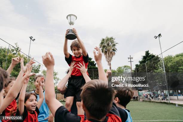 groep van kinderen vieren samen met de coach het winnen van een competitie op een voetbalveld - holding trophy stockfoto's en -beelden