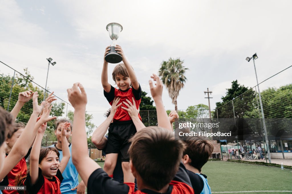 Group of kids celebrating together with the coach the winning of a competition on a soccer field