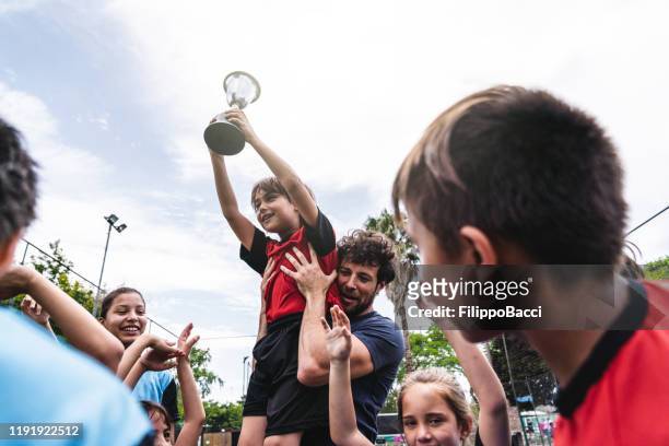 grupo de miúdos que comemoram junto com o ônibus a vitória de uma competição em um campo de futebol - the championship soccer league - fotografias e filmes do acervo