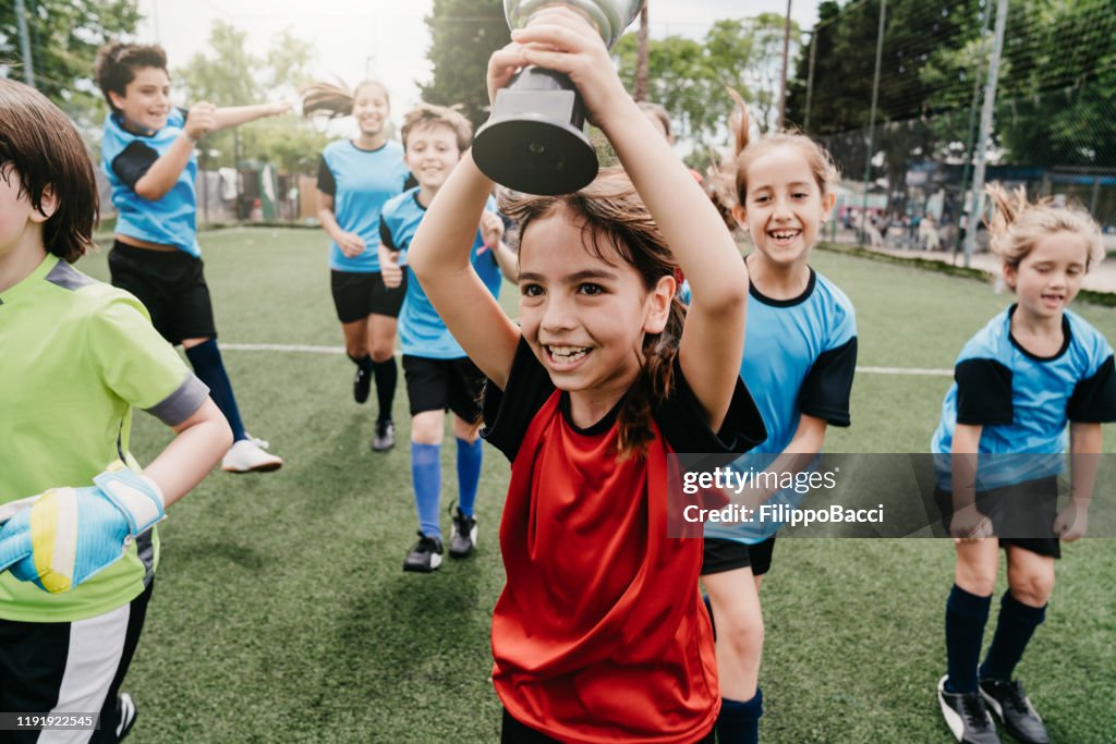 Grupo de niños celebrando juntos la victoria de una competición que corre en un campo de fútbol