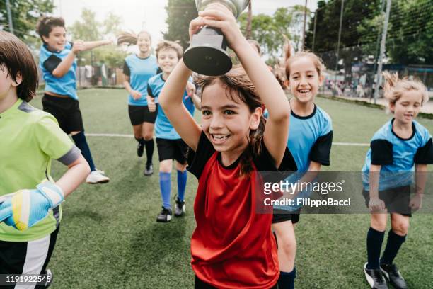 grupp barn firar tillsammans vinnande av en tävling som körs på en fotbollsplan - fotbollsmästerskap bildbanksfoton och bilder