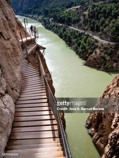 hikers in the nature walking on a wooden footbridge, nailed on the walls of rock in a gorge to great height. - caminito del rey málaga province stock pictures, royalty-free photos & images
