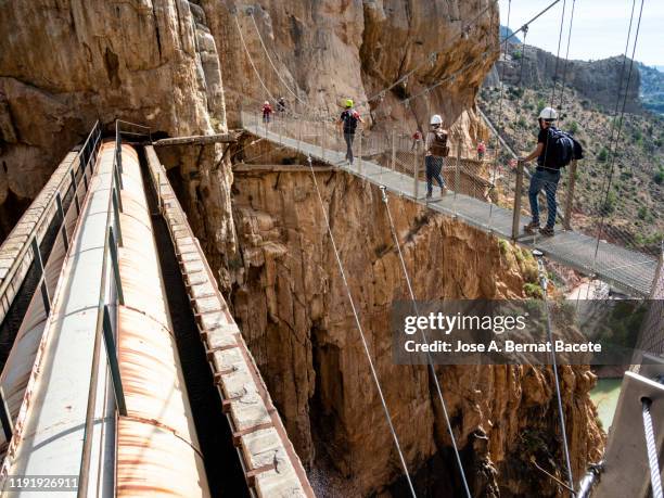 hikers in the nature walking on a wooden footbridge, nailed on the walls of rock in a gorge to great height. - caminito del rey fotografías e imágenes de stock