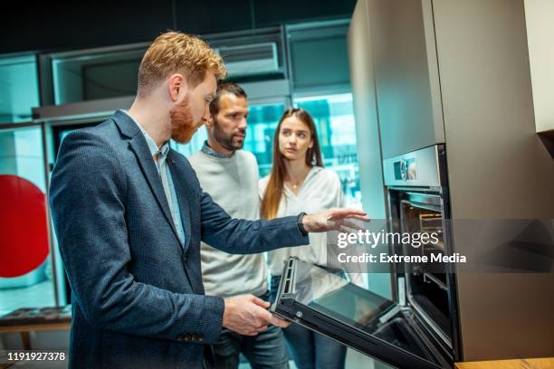 vertriebsmitarbeiter zeigt einem jungen paar in einem küchengerätegeschäft die eigenschaften eines modularen backofens - küchenzubehör stock-fotos und bilder