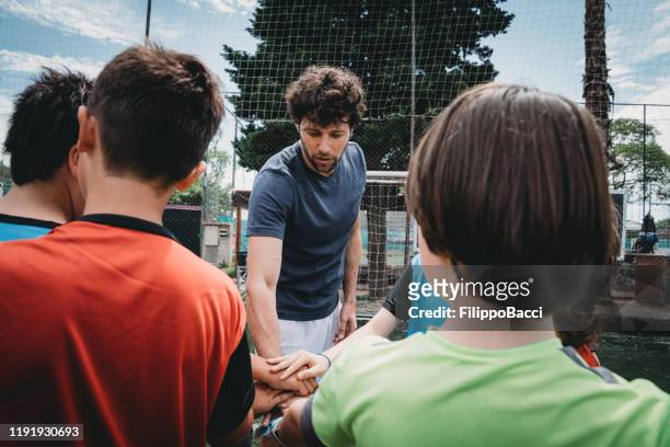 kids football school team huddling zusammen mit dem trainer auf einem fußballplatz - mannschaftsfußball stock-fotos und bilder