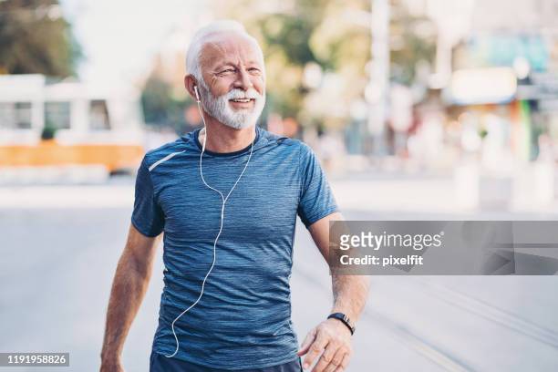 sportivo anziano sorridente che cammina per strada - beard men street foto e immagini stock
