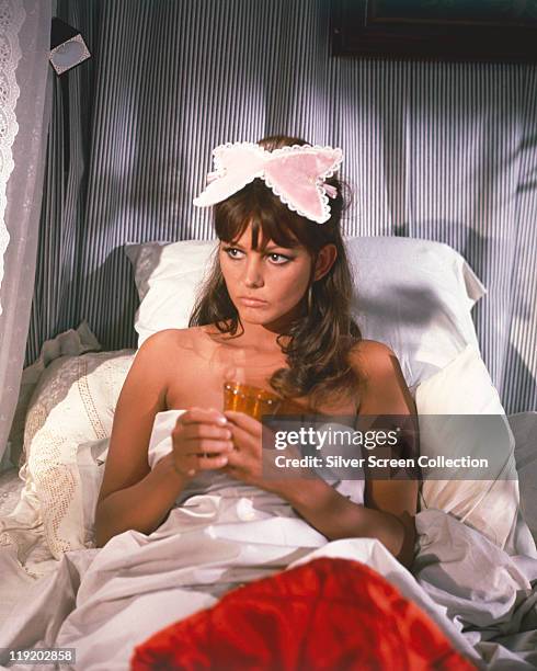 Claudia Cardinale, Italian actress, in bed holding a drink with a sleepmask on her head, circa 1960.