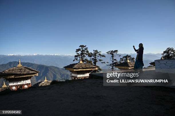 This photo taken on December 6, 2019 shows a tourist taking pictures of the "Druk Wangyal Chortens" stupas, with the Bhutanese Himalayas in the...