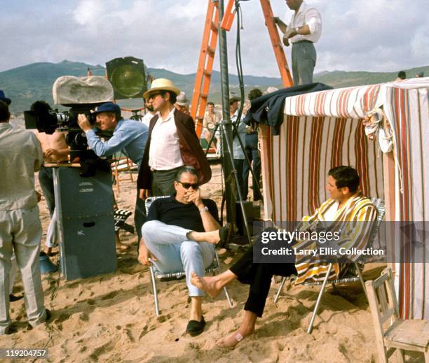 Australian actor George Lazenby sitting on a beach with producer Albert R. Broccoli during the filming of the James Bond film 'On Her Majesty's...