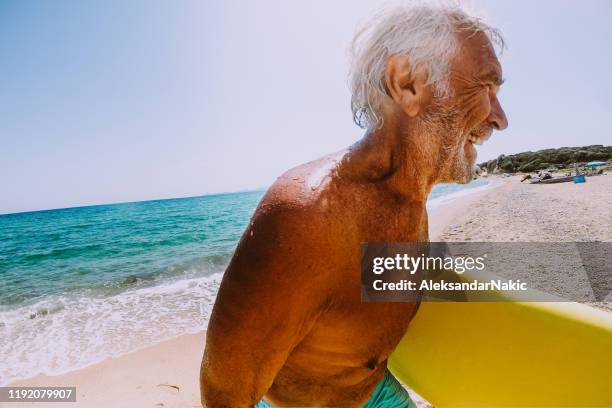 senior activo que lleva su tabla de surf - disruptagingcollection fotografías e imágenes de stock