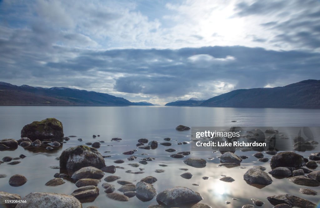 A view across Loch Ness looking down the length of the lake with rocks inn the foreground and dark clouds above, in Scotland