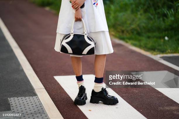 Guest wears a black and white Prada bowling bag, white socks with black and pink stripes, shiny patent leather platform lace-up shoes, outside the...