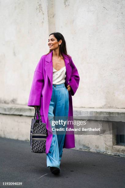 Sofya Benzakour wears earrings, a lustrous cream-color top with an embroidered neckline, a light purple coat, lustrous blue wide-legs full length...