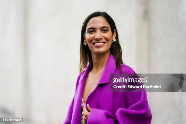Sofya Benzakour wears earrings, a lustrous cream-color top with an embroidered neckline, a light purple coat, lustrous blue pants, outside the Prada...