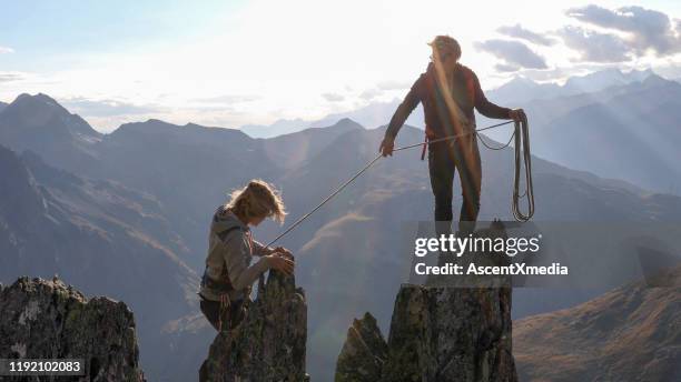 female mountaineer scrambles up mountain ridge - team climbing up to mountain top stock pictures, royalty-free photos & images