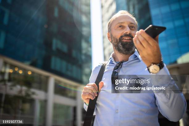 joyful mature man using cellphone on the street - voice command stock pictures, royalty-free photos & images