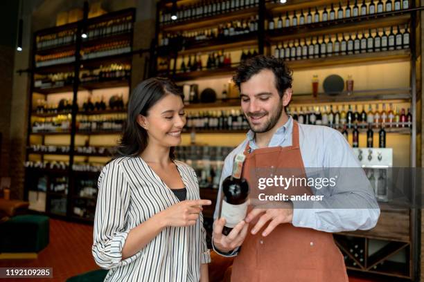 woman at a cellar asking sommelier about a bottle of wine - sommelier stock pictures, royalty-free photos & images