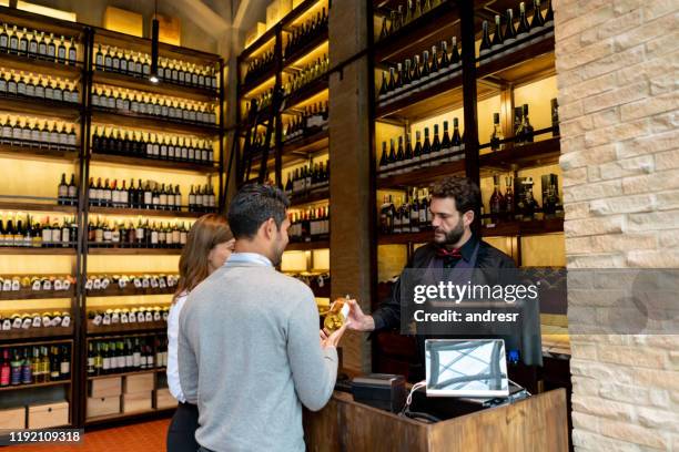 couple paying for a bottle of wine at a cellar - restaurant hostess stock pictures, royalty-free photos & images