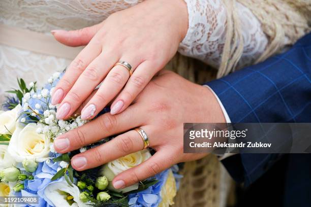 hands of the bride and groom on the wedding bouquet. gold wedding rings on the ring fingers of the newlyweds. - wedding ceremony stock pictures, royalty-free photos & images