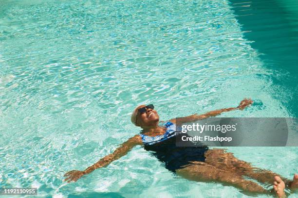 a mature woman relaxes in a swimming pool - summer pool stock pictures, royalty-free photos & images