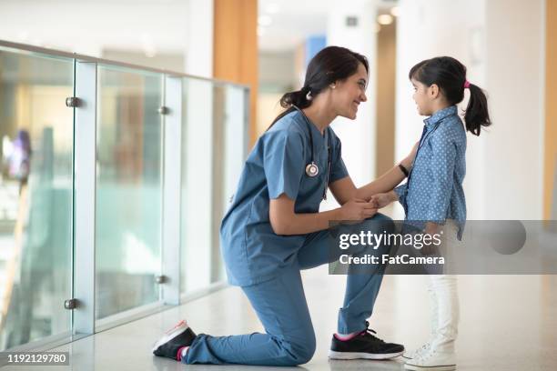 female doctor bends a knee to talk to little girl stock photo - afghan ethnicity imagens e fotografias de stock