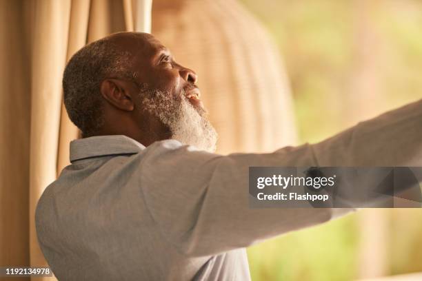 mature man opens curtains - drapeado stock pictures, royalty-free photos & images