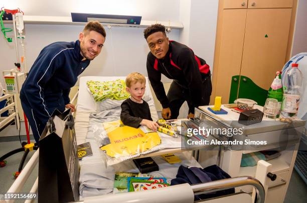 Raphael Guerreiro and Dan-Axel Zagadou of Borussia Dortmund pose with a kid during the annual visit at the Children's Hospital on December 04, 2019...