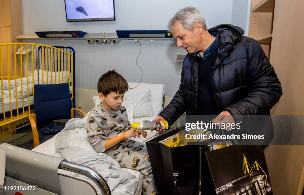 Head coach Lucien Favre of Borussia Dortmund hands over gifts to a kid during the annual visit at the Children's Hospital on December 04, 2019 in...